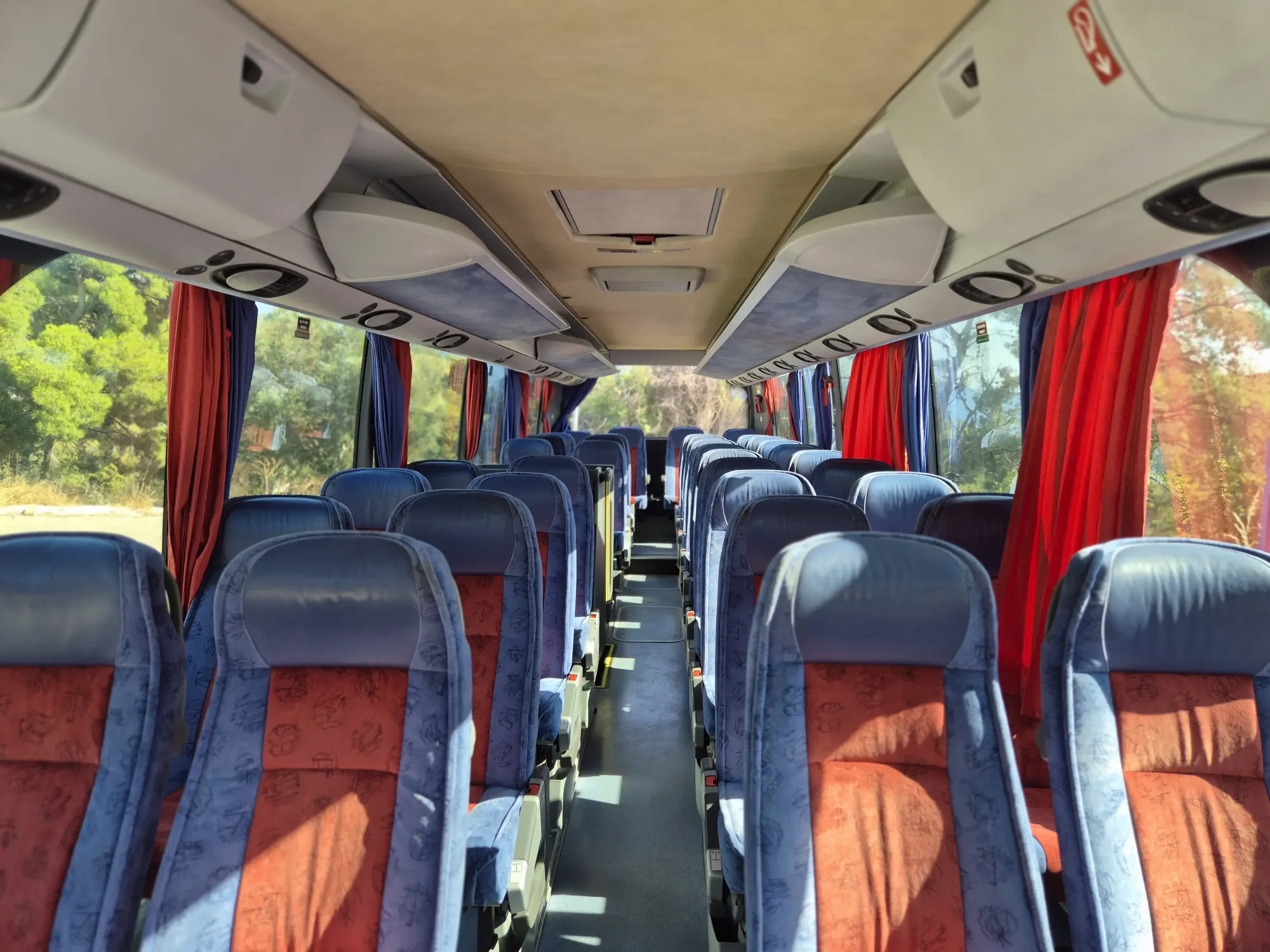Interior of a group coach with rows of blue and red reclining seats for transfers on Hvar
