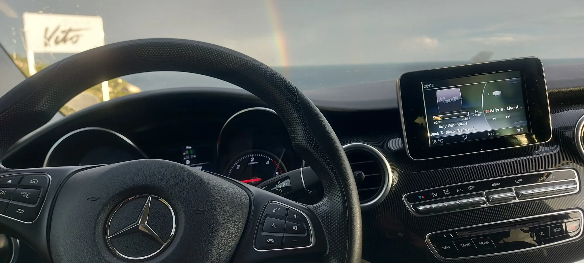 Luxury van cockpit with leather steering wheel and infotainment screen, sea and rainbow through the windscreen