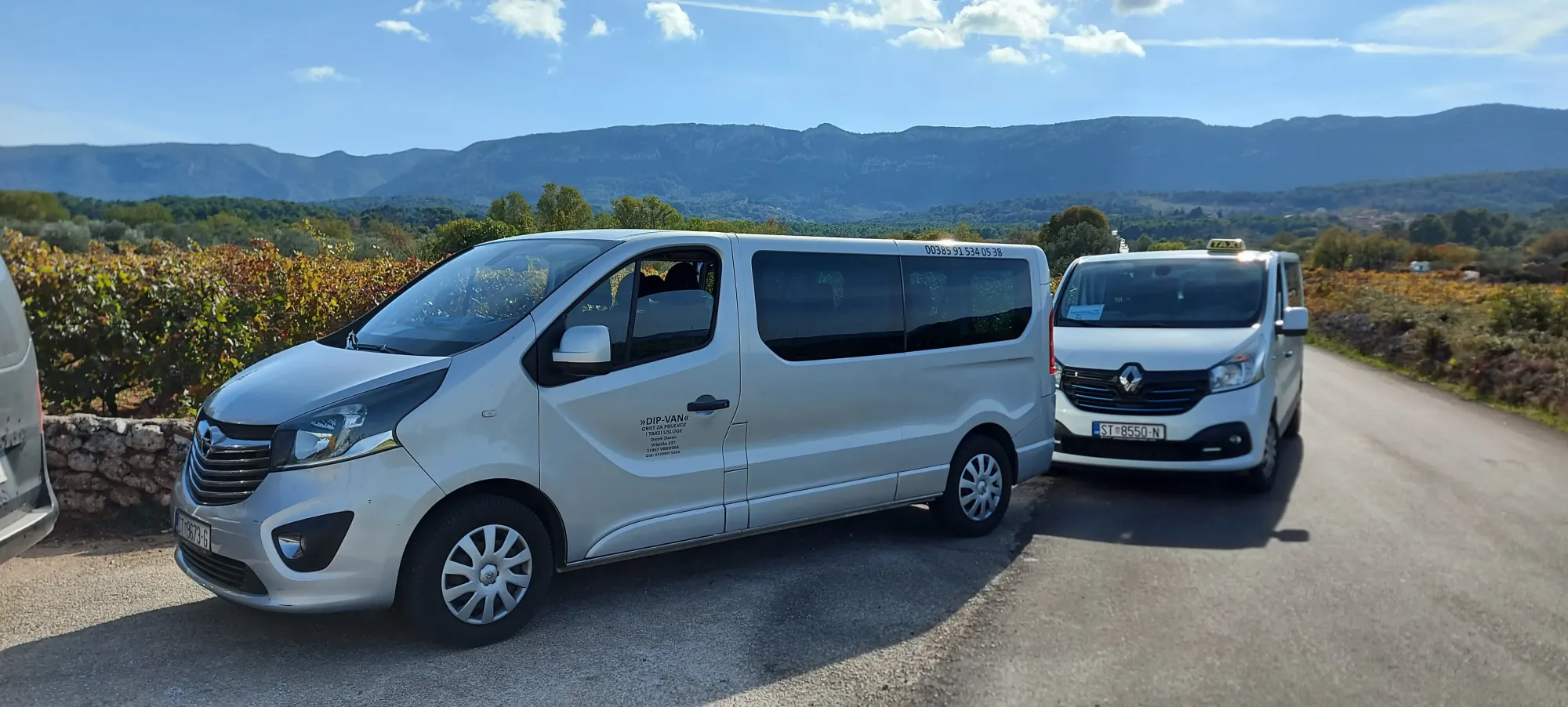 Silver Hvar taxi van and a car parked among vineyards with mountains behind on a wine trip