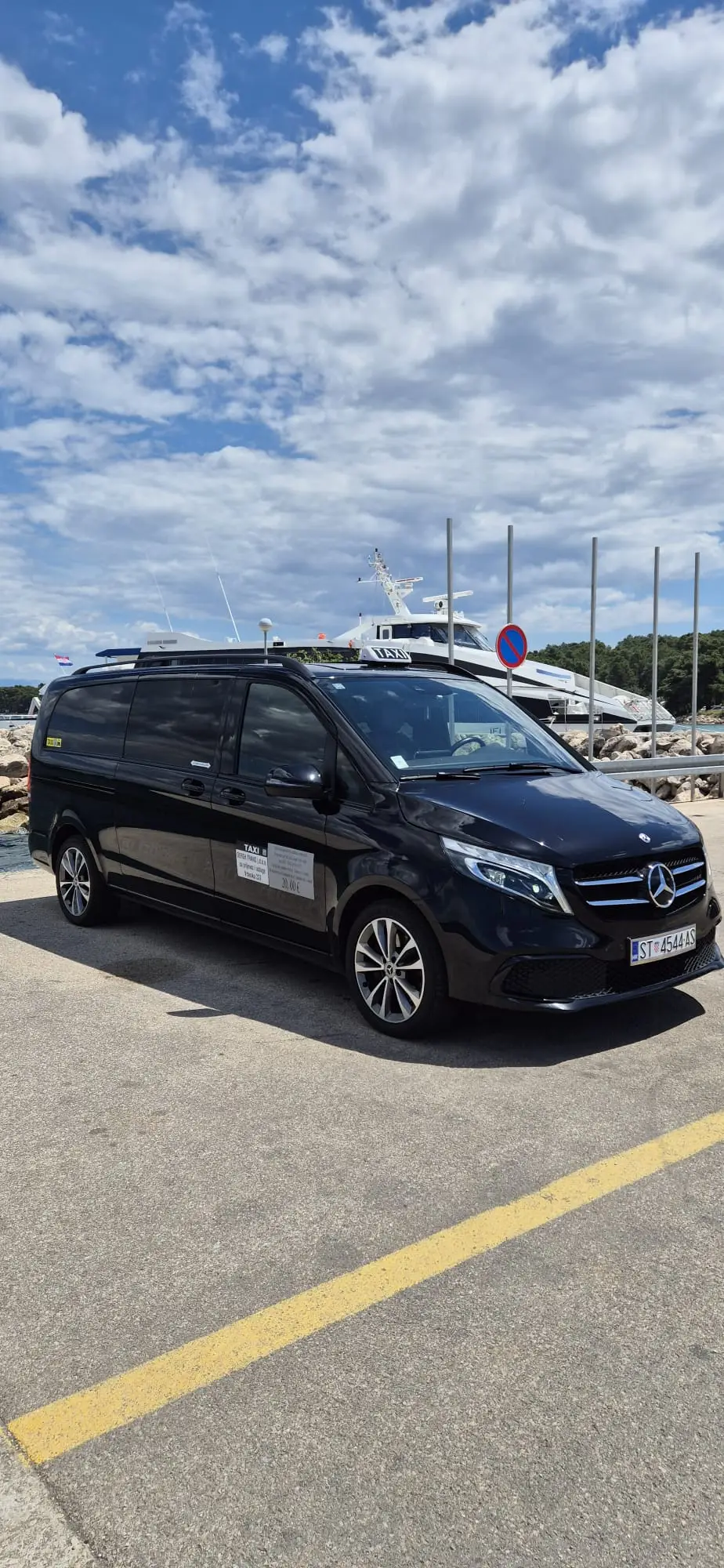 Black luxury van taxi in three-quarter side view on a Hvar harbour quay with yachts behind